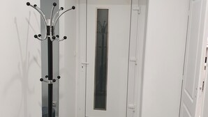 A hallway with a coat rack, a door with a frosted glass panel, and a white wall with a vent.