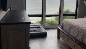 Un dormitorio con un ventanal grande que ofrece vistas al mar, una cama, un armario de madera y una pequeña zona de estar.