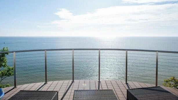 Una terraza con vista al mar, barandillas de metal y dos sillas de mimbre.