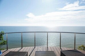 Een terras met uitzicht op zee, metalen hekwerk en twee rieten stoelen.