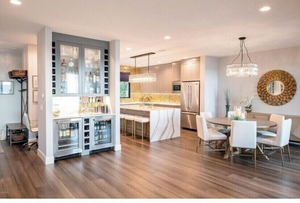 Una cocina moderna con barra integrada, un comedor con mesa redonda y sillas, y un espejo grande en la pared.