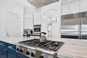 Una cocina moderna con estufa de acero inoxidable, muebles blancos y encimera de mármol.
