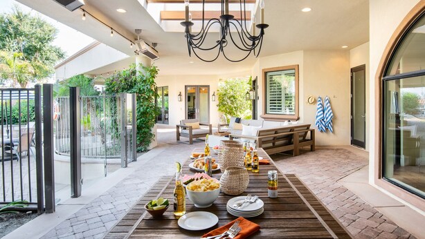 Un espace de restauration en plein air avec une table en bois dressée pour un repas, entourée de chaises et d’un canapé.