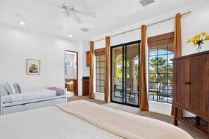 Un dormitorio con cama, ventilador de techo, ventana grande con cortinas y vistas al exterior.
