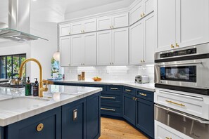 Una cocina moderna con armarios superiores blancos, un mueble inferior azul, electrodomésticos de acero inoxidable y encimera de mármol.