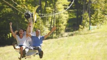 Eine Person auf einer Zipline, im Hintergrund eine Wiese und Bäume.
