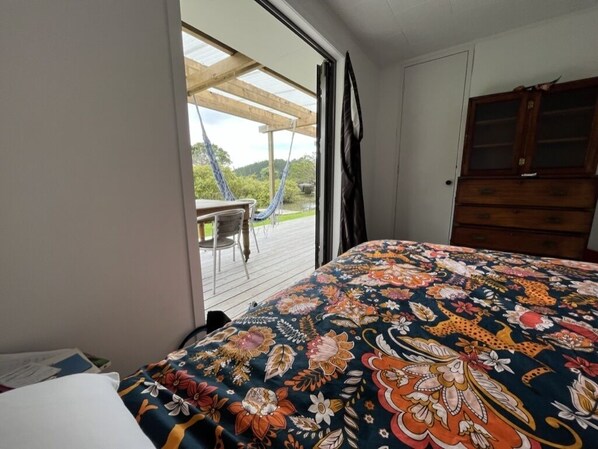 Une chambre à coucher avec un lit, une commode en bois et une vue sur un jardin, visible à travers une porte vitrée.