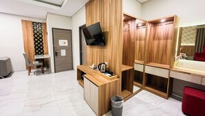 A hotel room with a wooden desk, a TV mounted on the wall, a red chair, a small trash bin, and a mirror. - Front One The Andia Boyolali (Boyolali)