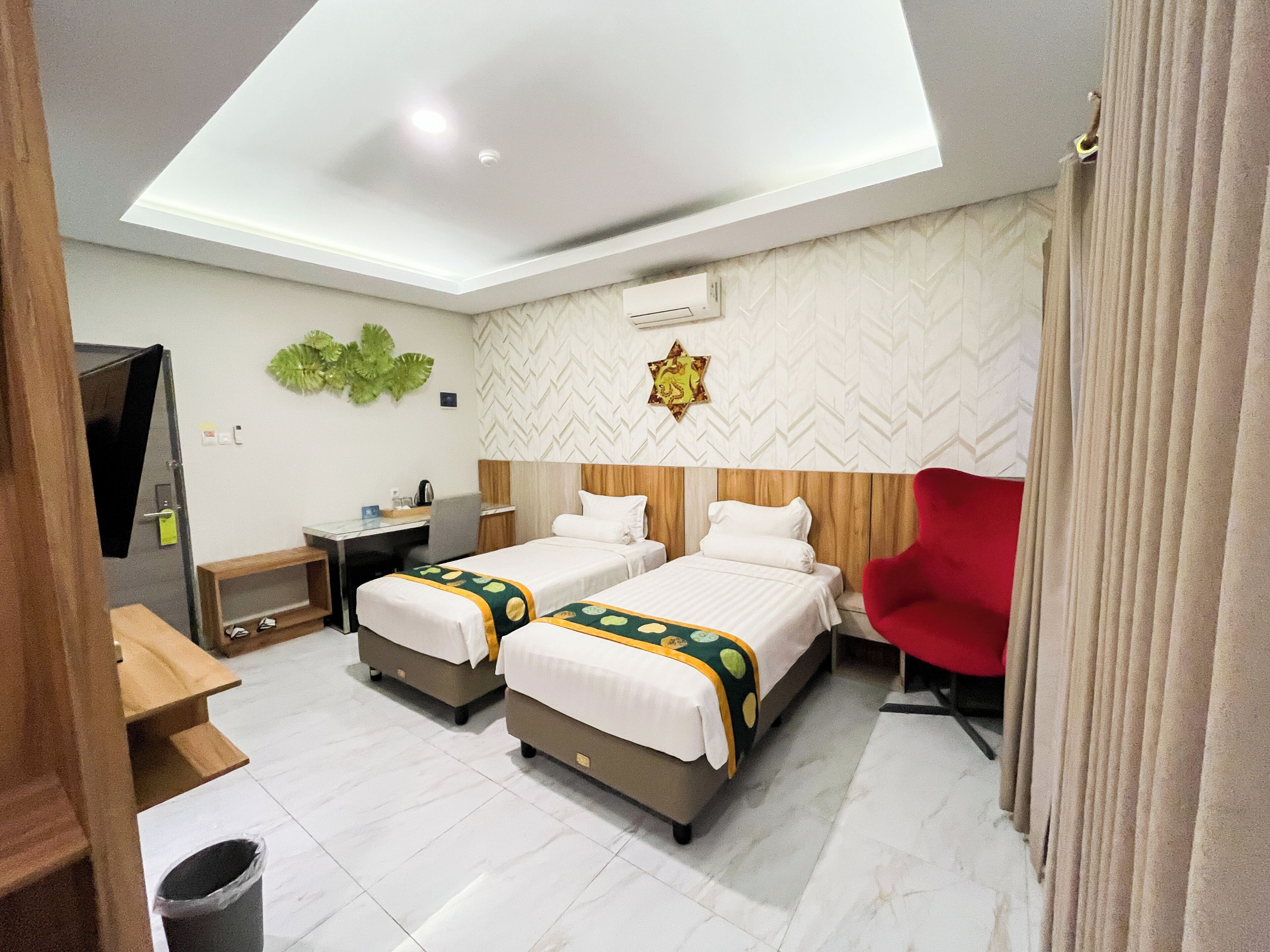 A hotel room with two beds, a desk, a chair, and a ceiling light.