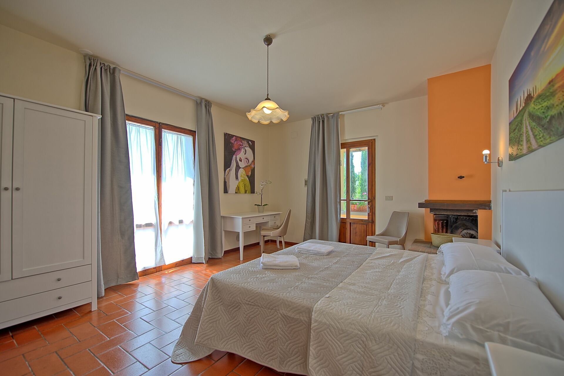 Een slaapkamer met een bed, een bureau, een stoel, een kledingkast en een open haard.