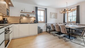 A modern kitchen with white cabinets, a wooden countertop, and a dining area with a table set for four. - Luxury chalet with private sauna (Donnersbachwald)