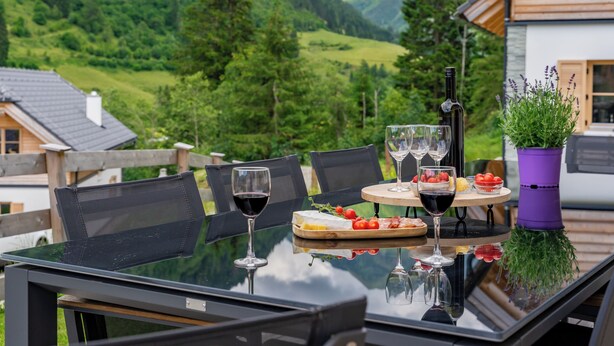 A dining table with chairs, a bottle of wine, and a bowl of fruit. - Luxury chalet with private sauna (Donnersbachwald)