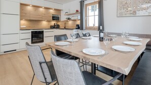 A modern kitchen with wooden cabinets, a dining table set for six, and a large antler chandelier. - Luxury chalet with private sauna (Donnersbachwald)