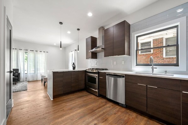 A modern kitchen with dark wood cabinets, stainless steel appliances, and a large window providing natural light.