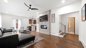 A modern living room with a black leather sofa, a coffee table, and a TV mounted on the wall. There is a staircase leading to another level. - " Top Notch House In Perfect Location" (Atlanta)