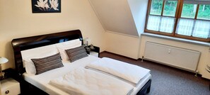 Une chambre à coucher avec un lit, une table de chevet, une lampe, un radiateur et une fenêtre avec des rideaux.
