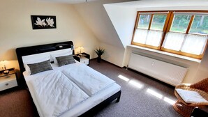 Une chambre à coucher comprenant un lit, des tables de chevet, un radiateur, une fenêtre avec des rideaux et un tableau accroché au mur.
