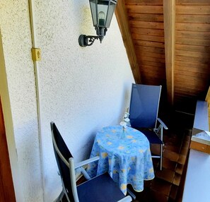 Ein kleiner Außenbereich mit Tisch und Stühlen, einer Wandleuchte und einer Holzbalkendecke.