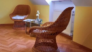 Une pièce avec deux fauteuils en osier, une petite table sur laquelle est posé un vase, et un radiateur.