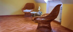 Une pièce avec deux fauteuils en osier, une petite table sur laquelle est posé un vase, et un radiateur.