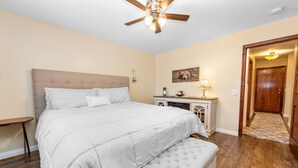 A bedroom with a large bed, a ceiling fan, a bedside table, a nightstand, a lamp, and a door. - Moose Tracks Lodge - Game Room, Ping Pong, Shuffleboard, Barbecue (Big Bear City)