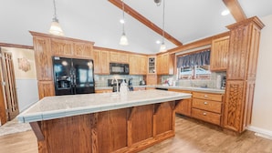 A kitchen with wooden cabinets, a large island, a refrigerator, and a microwave. - Moose Tracks Lodge - Game Room, Ping Pong, Shuffleboard, Barbecue (Big Bear City)