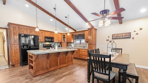 A spacious kitchen with wooden cabinetry, a central island, and a dining area with chairs. - Moose Tracks Lodge - Game Room, Ping Pong, Shuffleboard, Barbecue (Big Bear City)