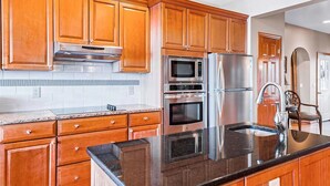 Eine moderne Küche mit Holzschränken, Edelstahlgeräten, Granitarbeitsplatten und einem eingebauten Backofen.