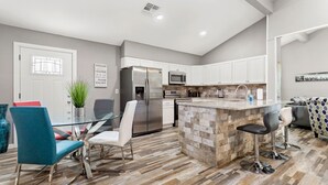 A modern kitchen with white cabinets, stainless steel appliances, and a herringbone wood floor.
