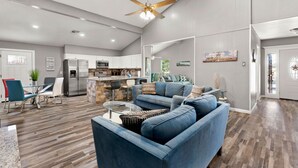 A spacious living area with a blue sofa, a dining table with chairs, and a kitchen in the background.