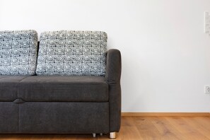 A grey sofa with patterned cushions against a white wall and wooden flooring.