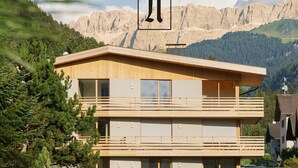 A modern two-story building with a wooden facade, large windows, and a balcony. - Holiday Apartment "Noreia Granda" with Mountain View, Pool, Wi-Fi, Terrace & Balcony (St.Ulrich)