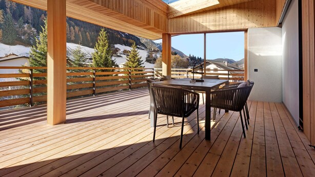 A wooden deck with a table and chairs, overlooking a snowy mountain landscape. - Holiday Apartment "Noreia Granda" with Mountain View, Pool, Wi-Fi, Terrace & Balcony (St.Ulrich)