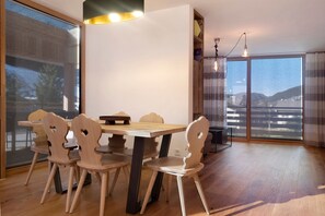 Uma sala de jantar com mesa e cadeiras de madeira, luminária pendente moderna e vista pela grande janela.