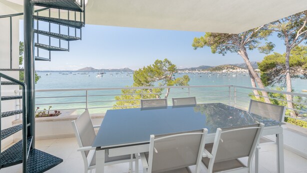 Un balcon avec une table et des chaises en verre, offrant une vue sur la côte, avec des bateaux et des arbres.