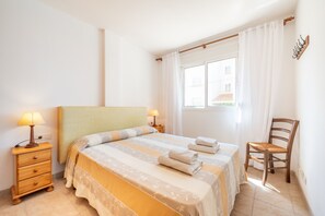 A bedroom with a bed, two bedside tables with lamps, a chair, and a window with curtains.
