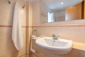A bathroom with a sink, mirror, towel rack, and a shower area.