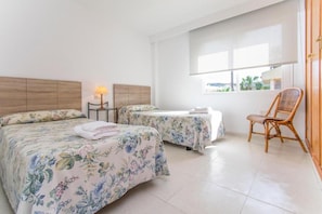 A hotel room with two beds, a chair, a lamp, and a window with a view.