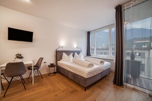 Une chambre à coucher avec un lit, un bureau, une chaise, une télévision et une grande fenêtre.