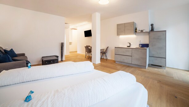Ein modernes Hotelzimmer mit einem großen Bett, einem Schreibtisch, einem Sessel, einem Fernseher und einer Küchenzeile.