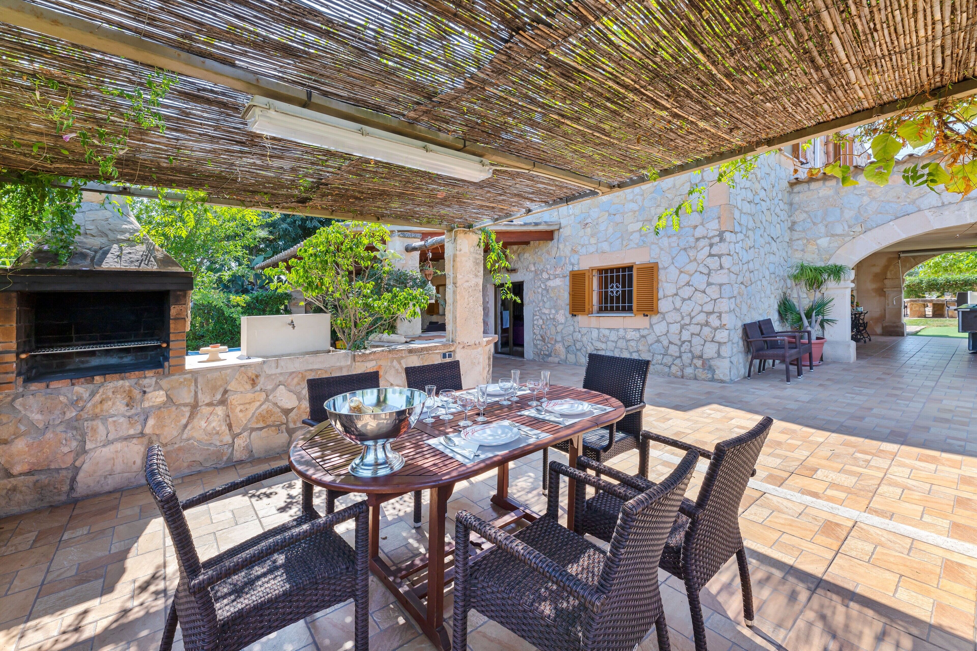 Un patio exterior con paredes de piedra, una parrilla, muebles de mimbre y una pérgola.