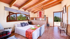 A bedroom with a bed, a table, and a chair. There is a window and a view of greenery outside. - Pet-friendly Villa Cala Veritat with Mountain View, Pool, A/C, Wi-Fi, Garden, Terrace & Balcony (inca)