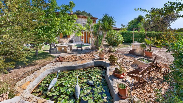 A garden with a pond, stone pathway, and rustic furniture. - Pet-friendly Villa Cala Veritat with Mountain View, Pool, A/C, Wi-Fi, Garden, Terrace & Balcony (inca)