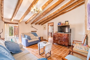 Una habitación acogedora con un sofá, una mesita, un armario de madera y un televisor.