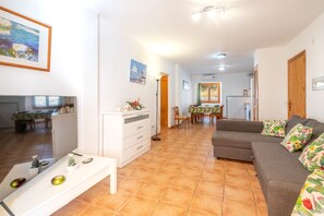 A living room with a sofa, a coffee table, a TV, and a dining area with a table and chairs.