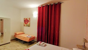 Una habitación pequeña con una cama individual, un armario, un cuadro en la pared y una ventana con cortinas rojas.