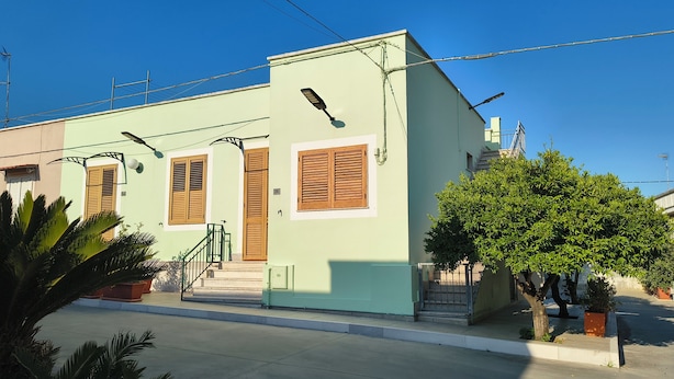 Un edificio de dos pisos con fachada verde, contraventanas de madera y un pequeño porche delantero.