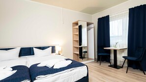 Ein Hotelzimmer mit einem Bett, einem Schreibtisch, zwei Stühlen, einem Spiegel und einem Fenster mit Vorhängen.