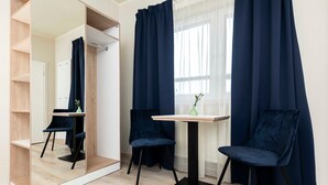 Ein Zimmer mit Spiegel, Tisch, zwei Stühlen, einem Fenster mit Vorhängen und Holzboden.
