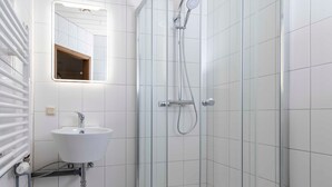 A bathroom with a white sink, a mirror, a shower with a glass door, and a towel rack.